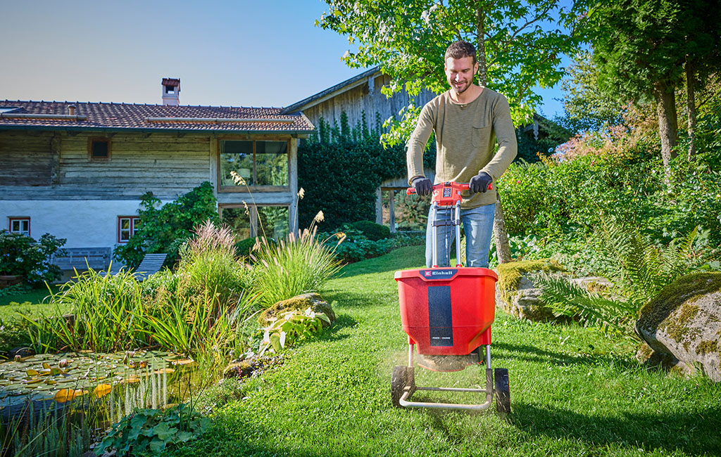 A man with an Einhell spreader spreading fertilizer in the garden