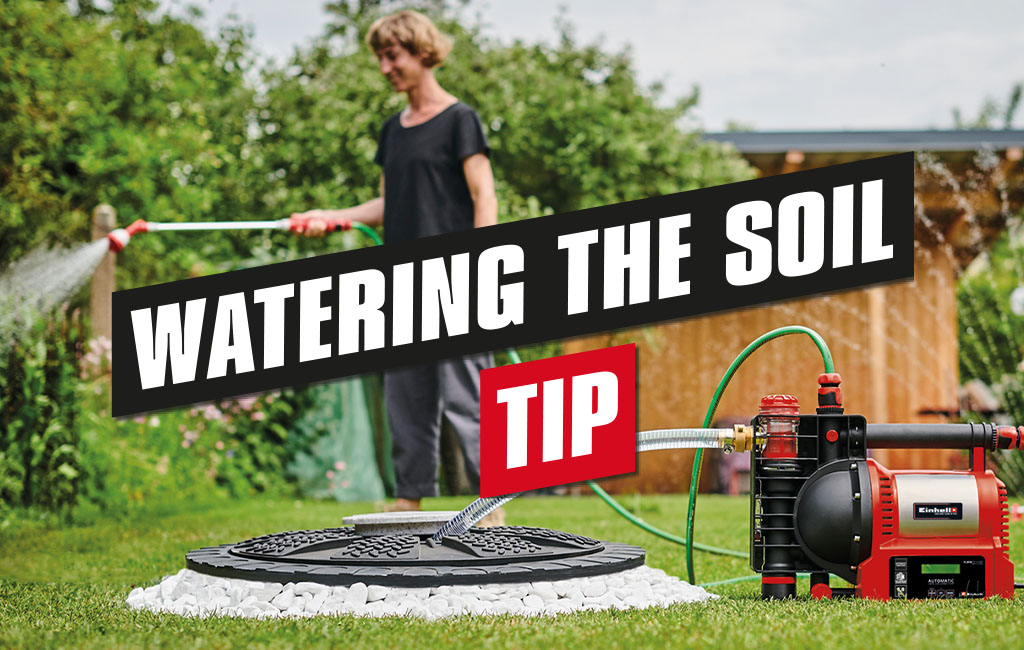 A woman waters her garden with the help of a garden pump. The text in the picture says: Watering the soil - tip.