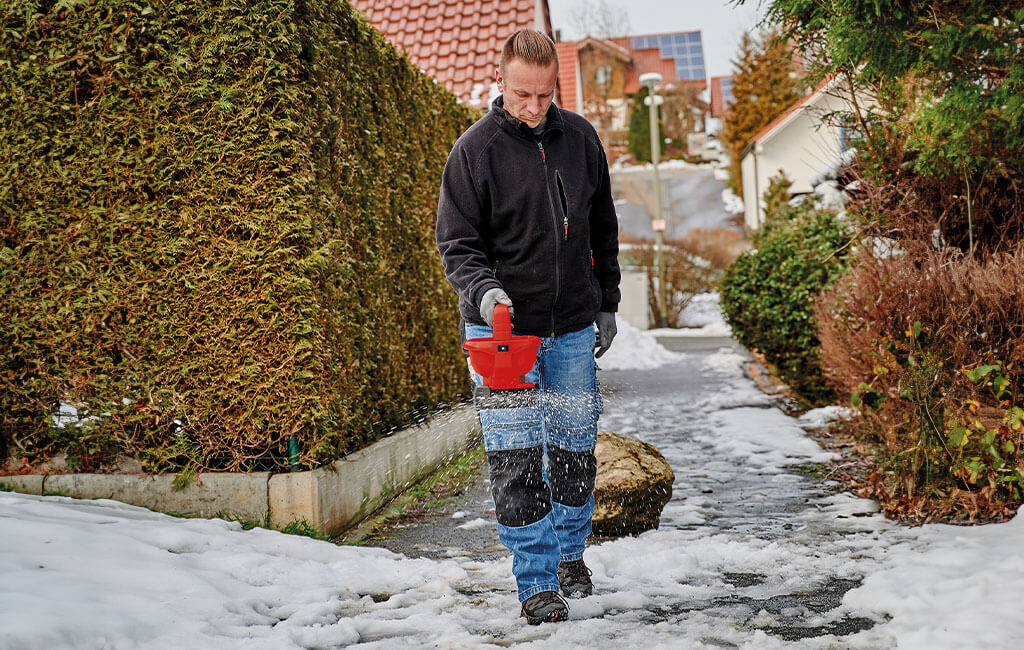 Mann beim Streuen eines vereisten Weges mithilfte eines Akku-Streuers und Streusalz