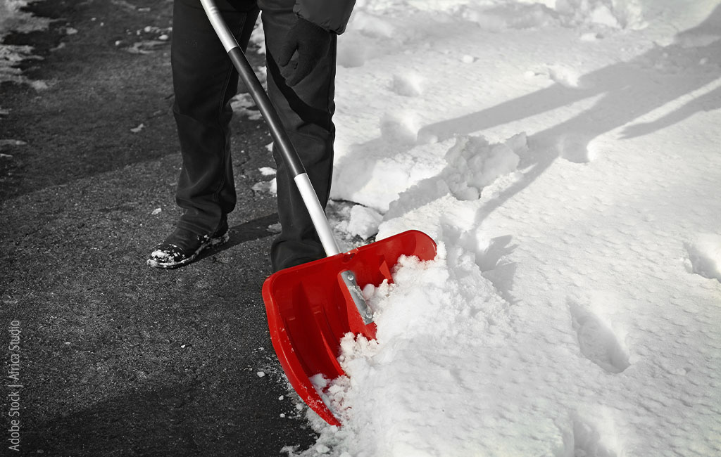 Schnee wird mit einer roten Schaufel von einer Straße geschippt