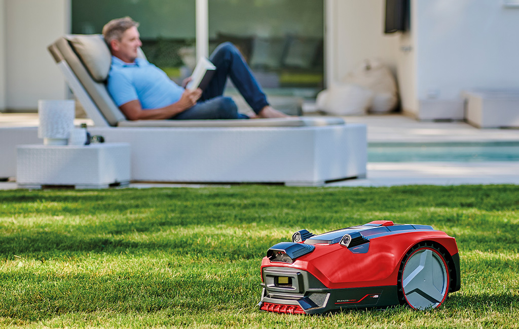 Einhell Mähroboter FREELEXO CAM mäht den rasen, während ein Mann auf einer Liege entspannt