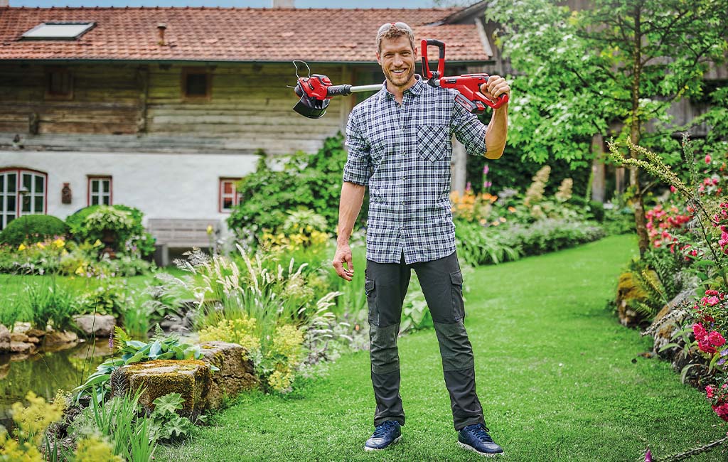 Ein Mann im Garten, auf seinen Schultern liegend hält er einen Akku-Rasentrimmer.