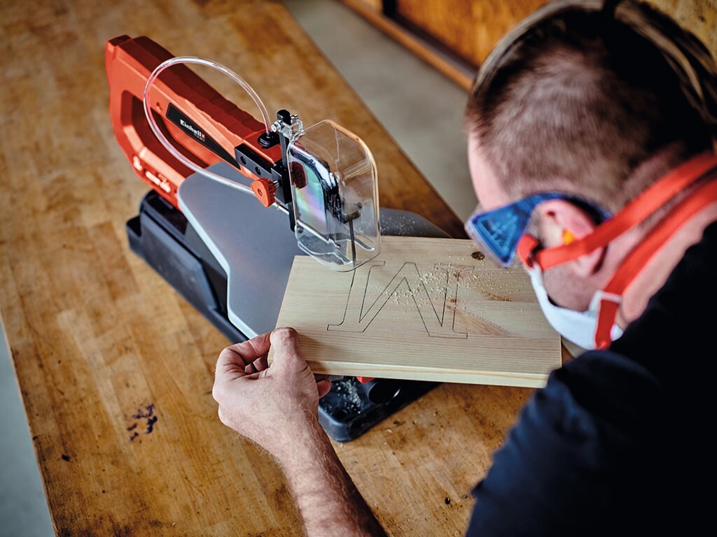 A man cuts an M out of a wooden board with a jigsaw