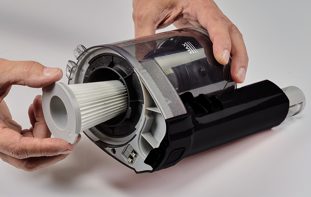 Detailansicht des geöffneten Motorgehäuses mit eingesetztem Filter und schwarzer Abdeckung in der Hand.