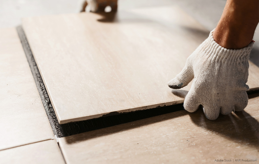 A craftsman places a new floor tile onto the prepared adhesive and aligns it.