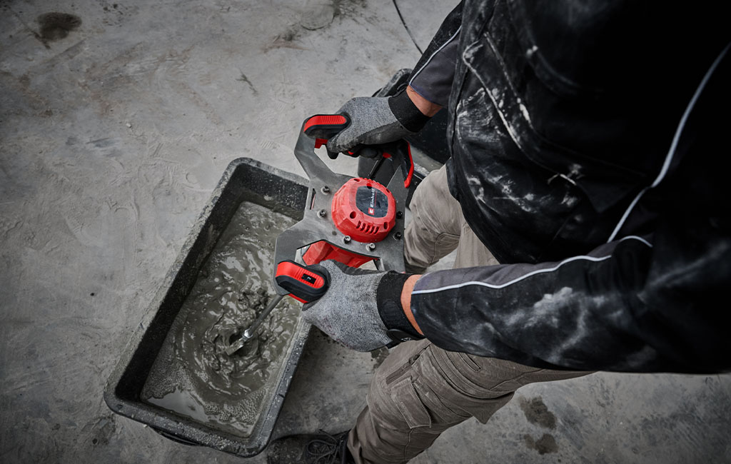 A craftsman mixes tile adhesive in a tub using an Einhell cordless paint and mortar mixer.