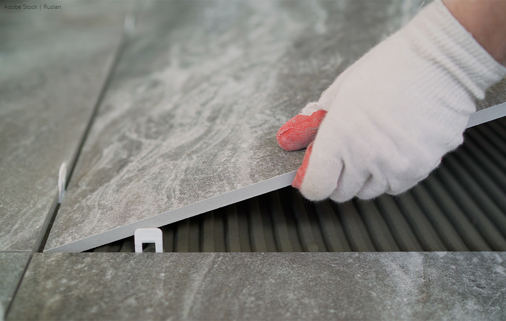 A new floor tile is placed onto the adhesive with tile spacers for precise alignment.