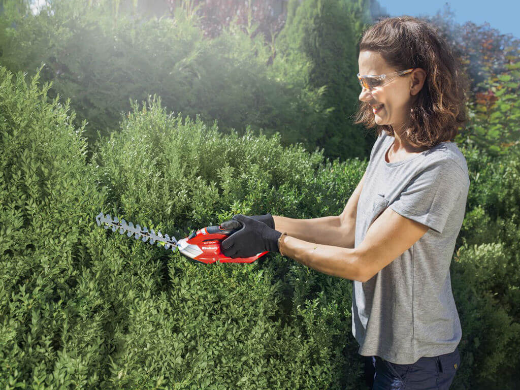 A woman cuts the hedge with a small hedge trimmer
