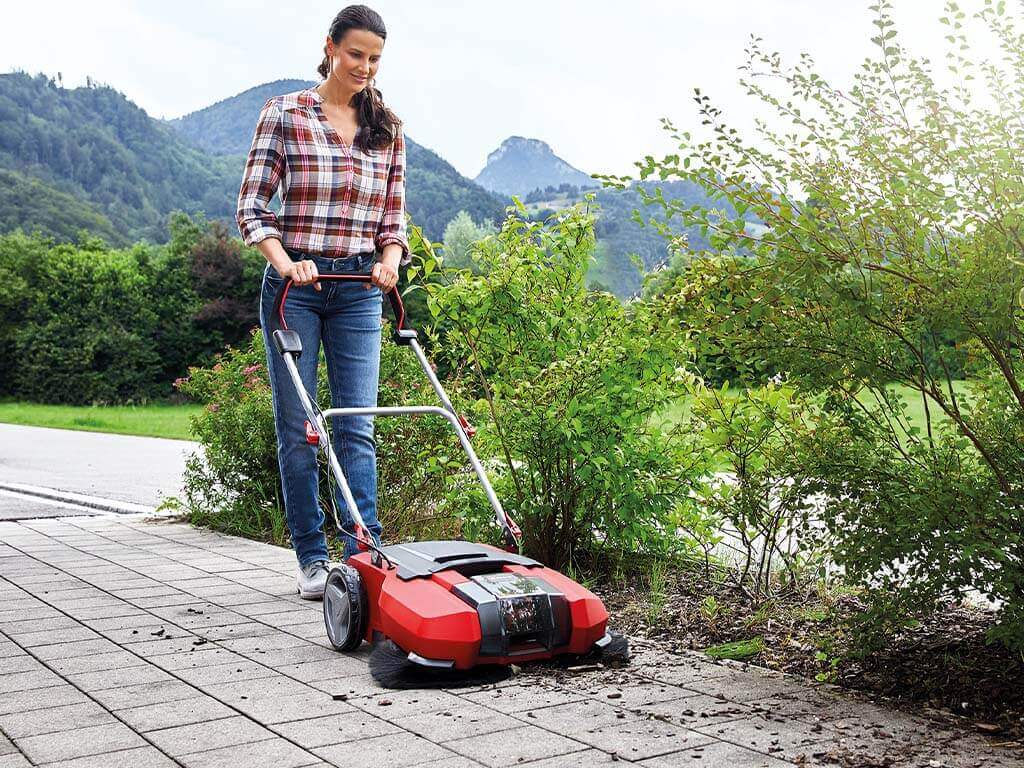 a woman sweeps the pavement with a sweeper