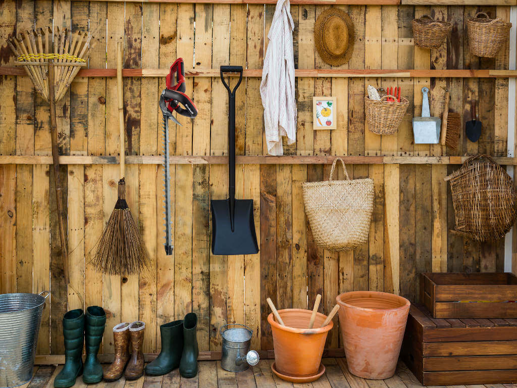 garden equipment leans and hangs on a wooden wall
