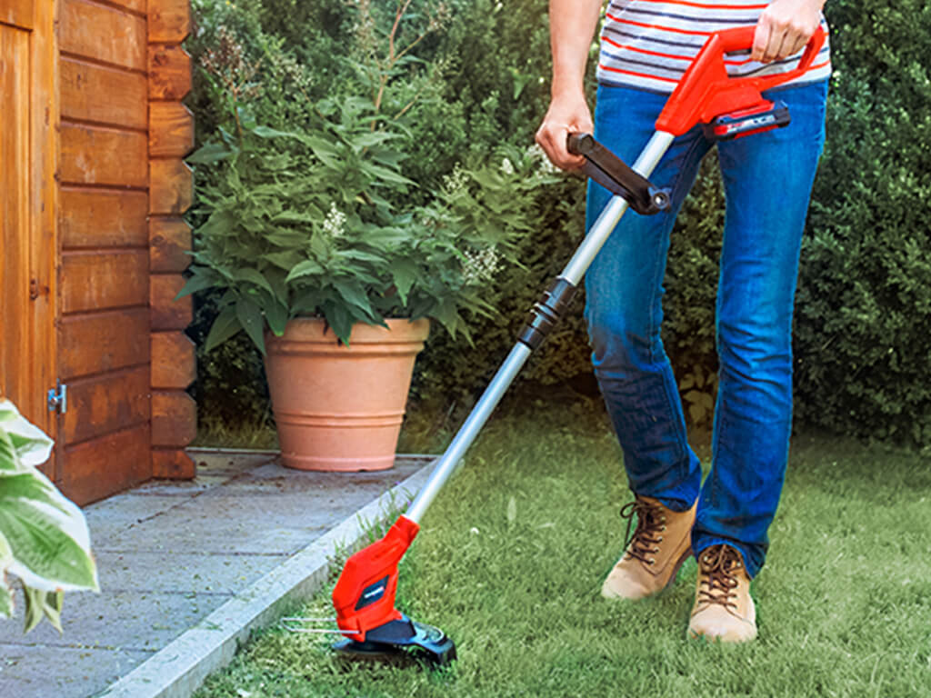 a woman trims the lawn next to a wooden hut