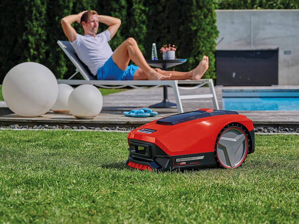A man lies on the lounger while the lawnmower robot mows the lawn