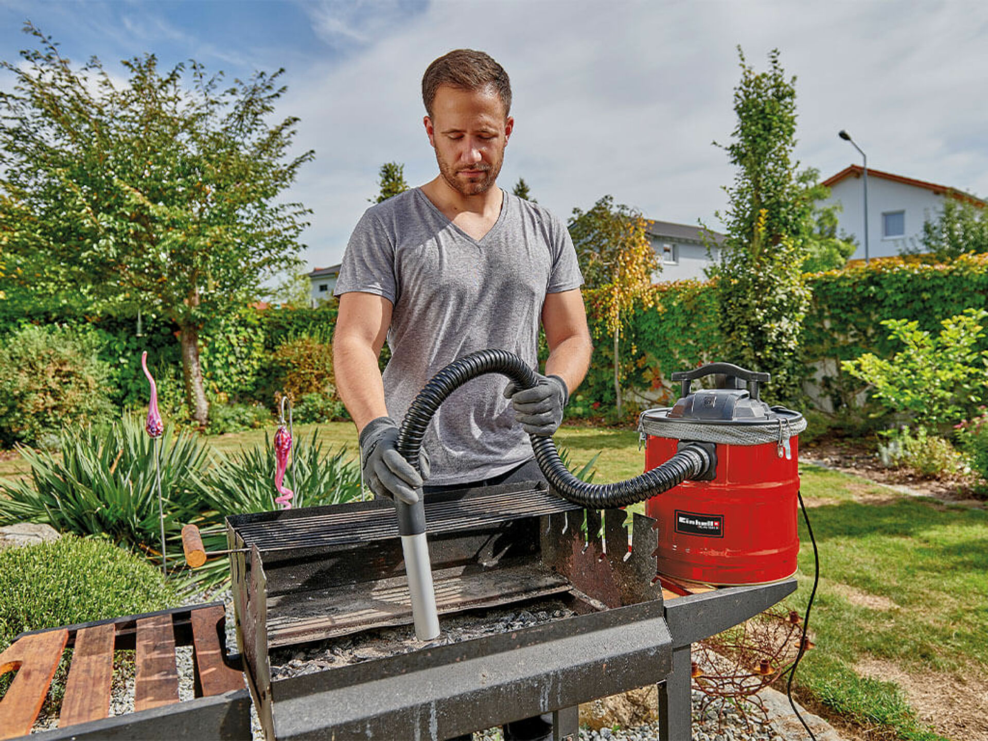 A man cleans his barbecue in the garden with a compact ash vacuum cleaner from Einhell.