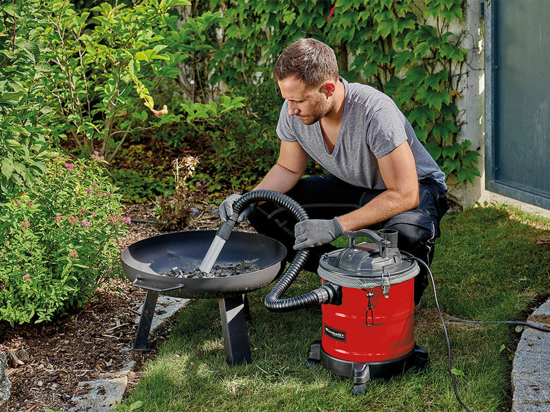 A man cleans his fireplace in the garden with the help of an Einhell ash vacuum cleaner.