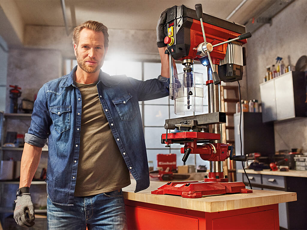 Man standing next to a workbench with a large Einhell bench drill.