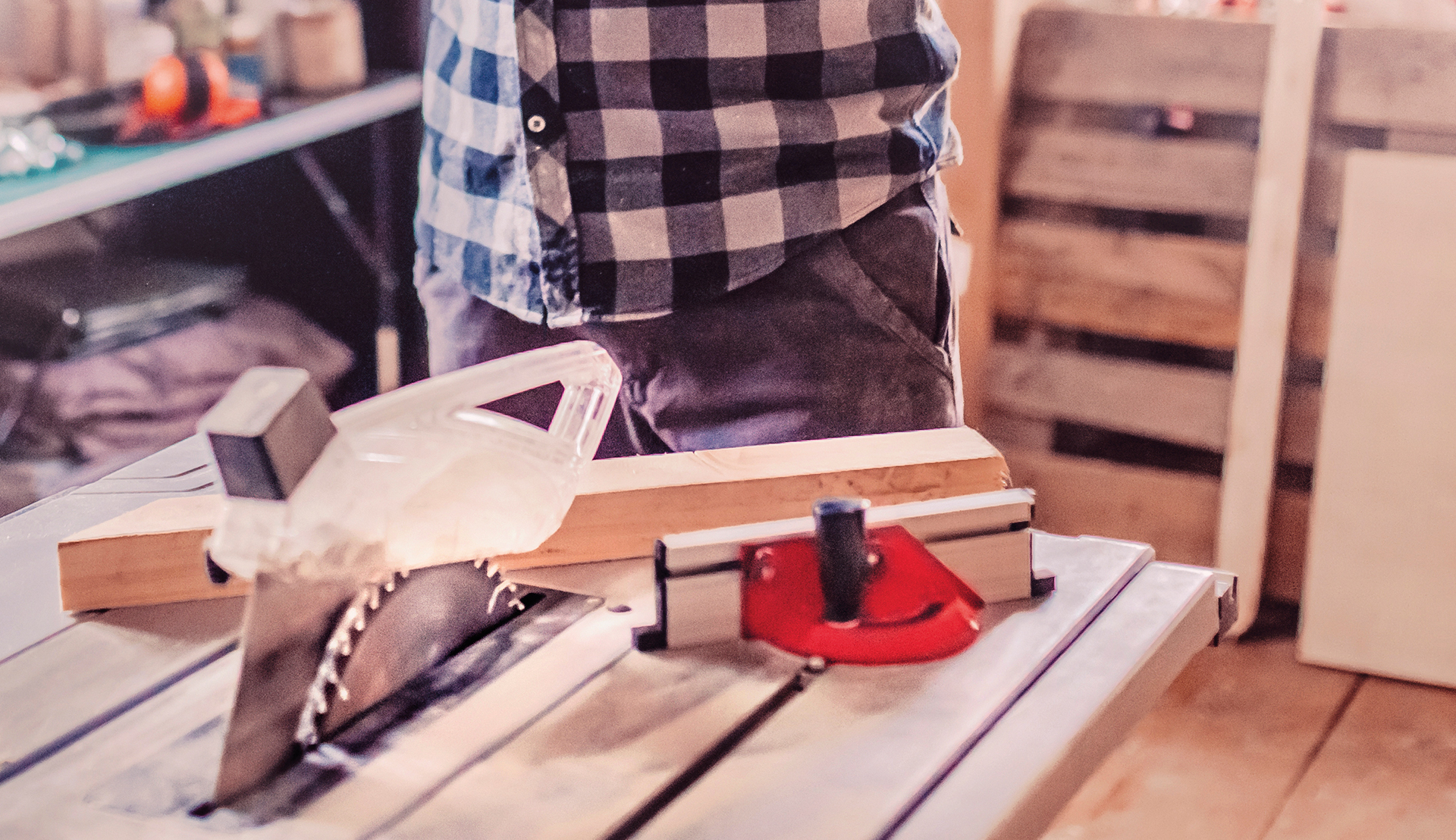 A person guiding a wooden board along the rip fence and across a table saw using a push stick.