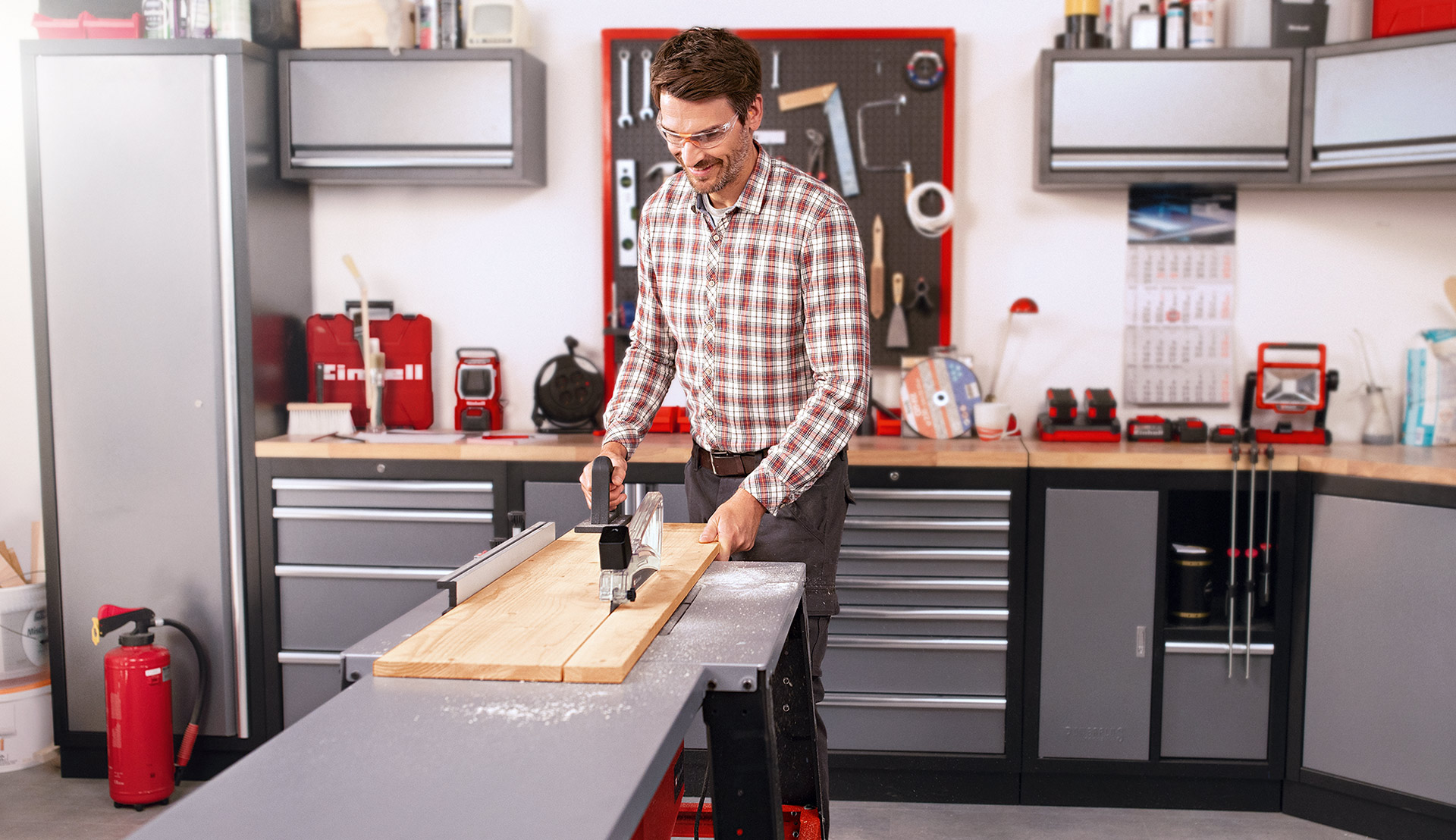 A man guiding a wooden board across a table saw in a workshop.
