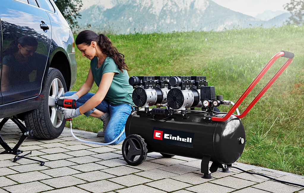 Eine Frau verwendet einen Einhell Kompressor, um die Reifen eines Autos aufzupumpen, während sie auf einer Auffahrt sitzt.