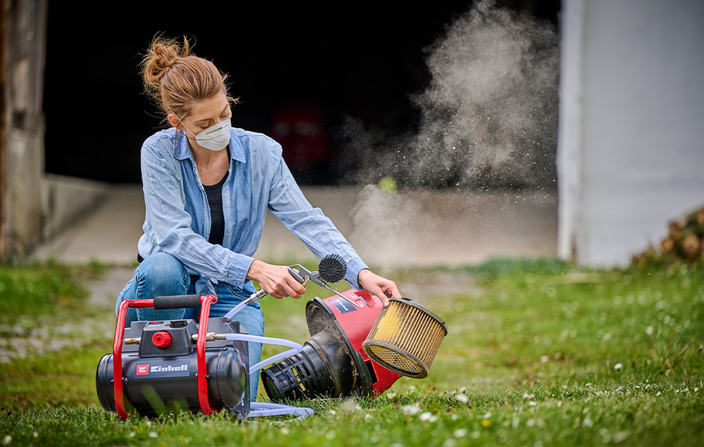 Eine Frau reinigt einen staubigen Filter mit einem Einhell Akku-Kompressor im Freien.