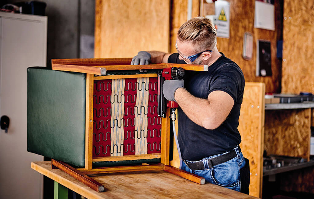 Ein Mann verwendet eine Druckluft-Tacker, um eine Sitzmöbelreparatur durchzuführen.
