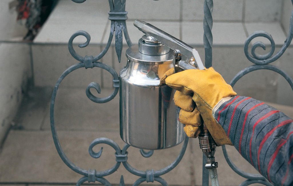 Eine Person sandstrahlt mit einer Strahlpistole eine Beschichtung auf ein Metallgeländer auf.