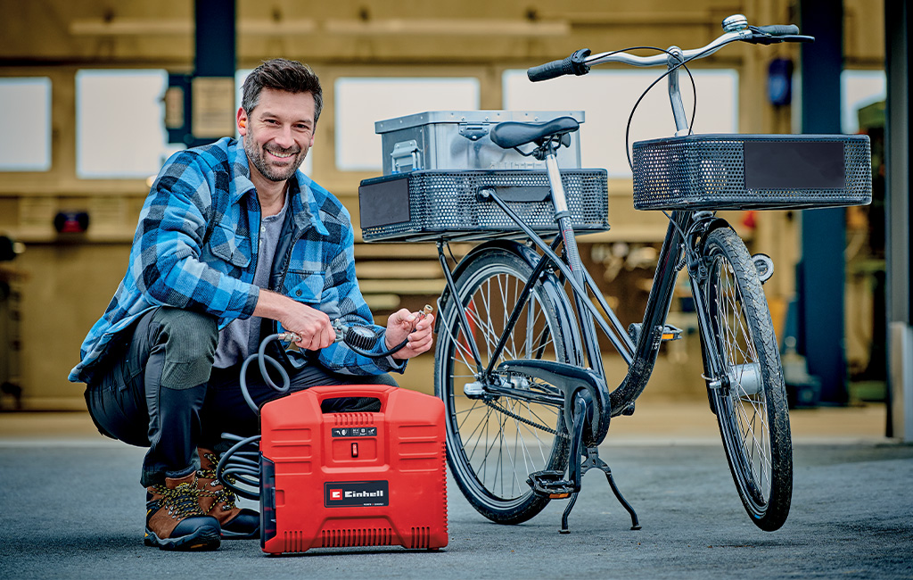 Ein Mann nutzt einen Einhell Koffer-Kompressor, um die Reifen eines Fahrrads in einer Werkstatt aufzupumpen.