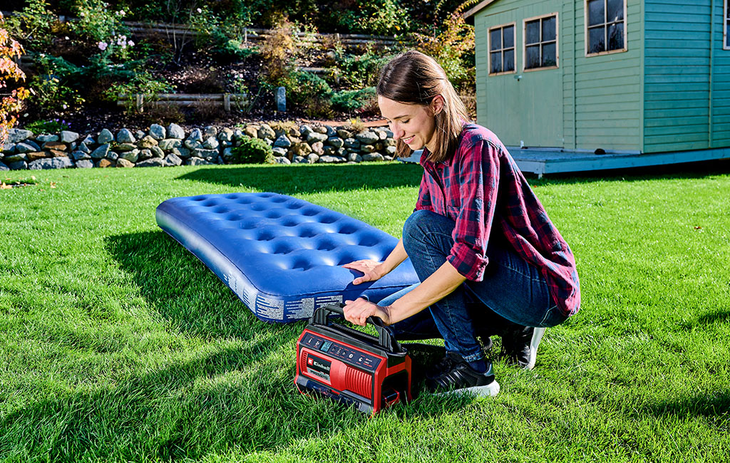 Eine Frau pumpt mit dem Einhell Akku-Kompressor PRESSITO eine Luftmatratze im Garten auf.
