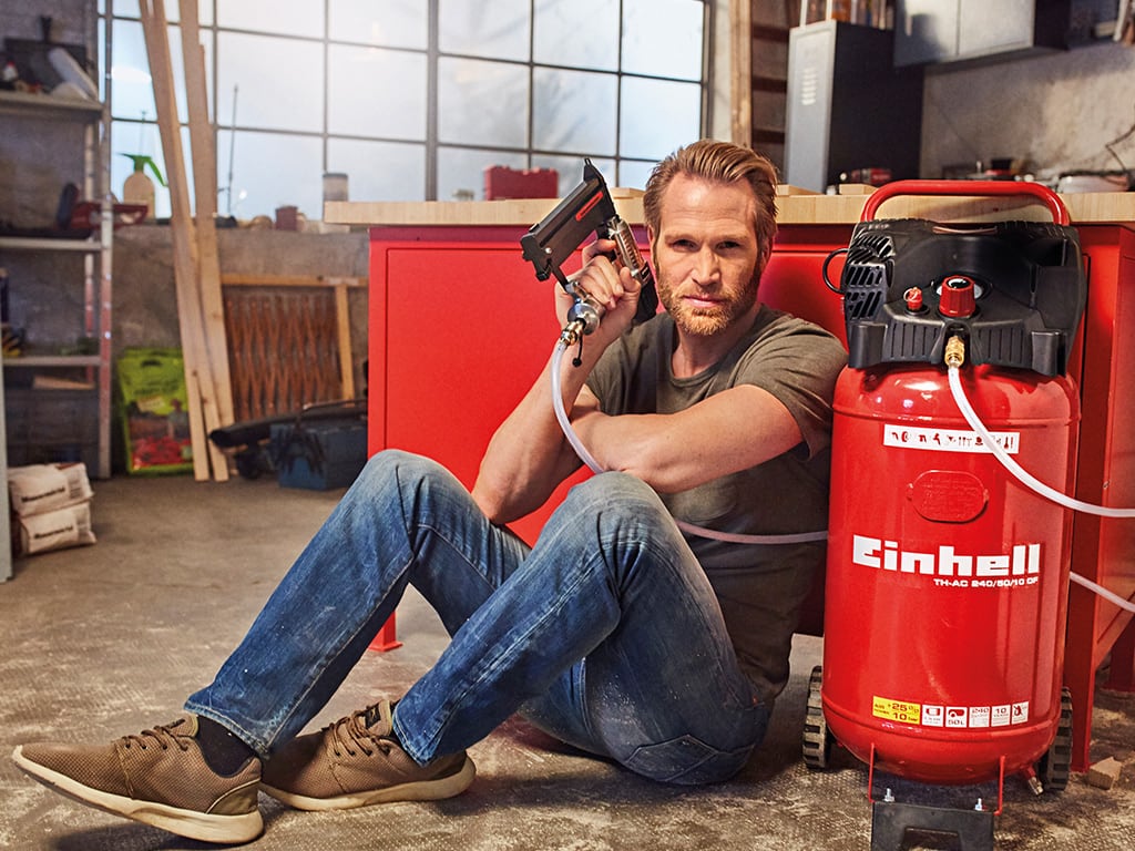 A man sits on the floor with a staple gun in his hand