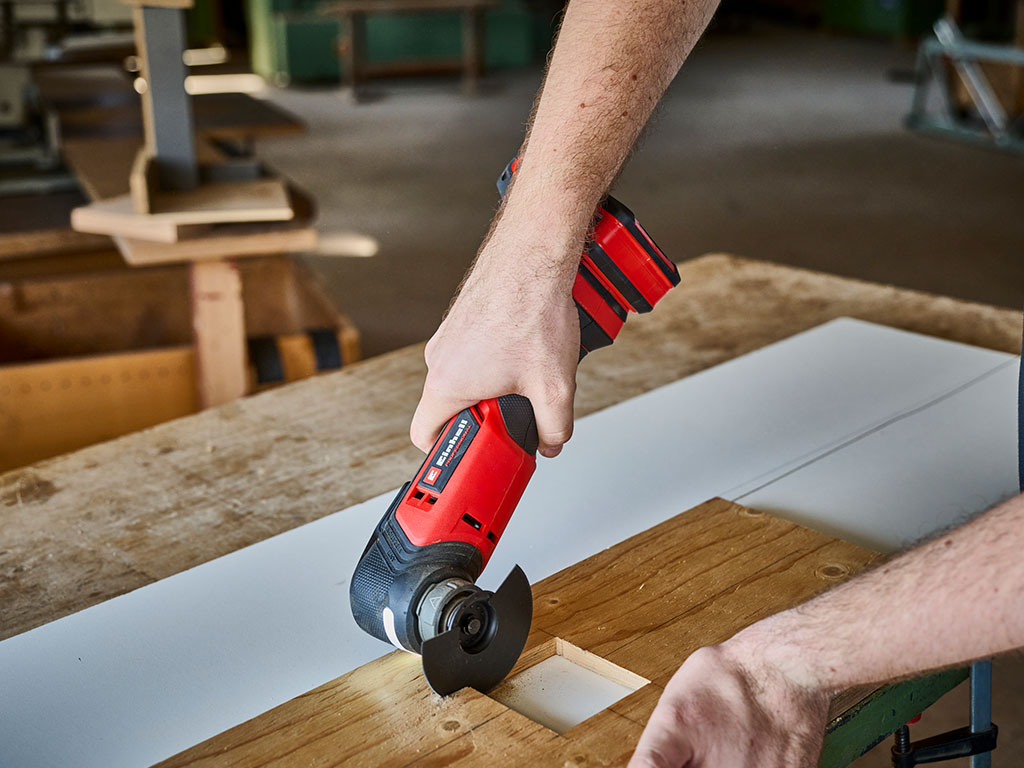 The Einhell multifunctional tool cuts into a wooden strip on a workbench.
