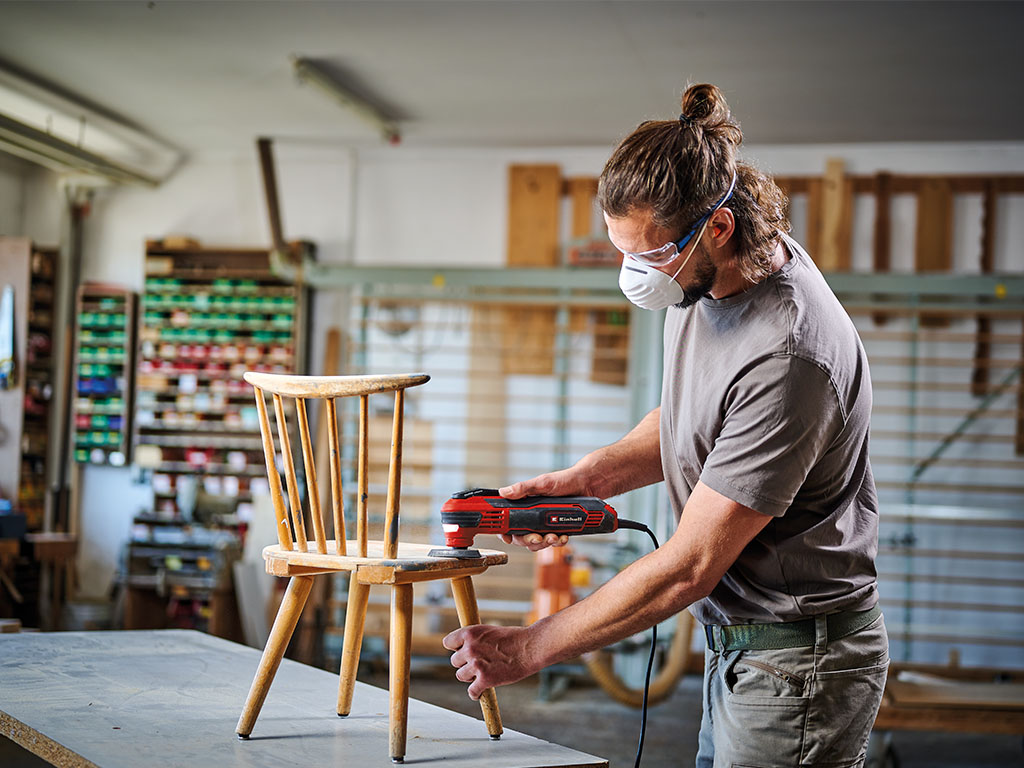 A man sands a wooden chair with the Einhell multifunctional tool in a workshop.