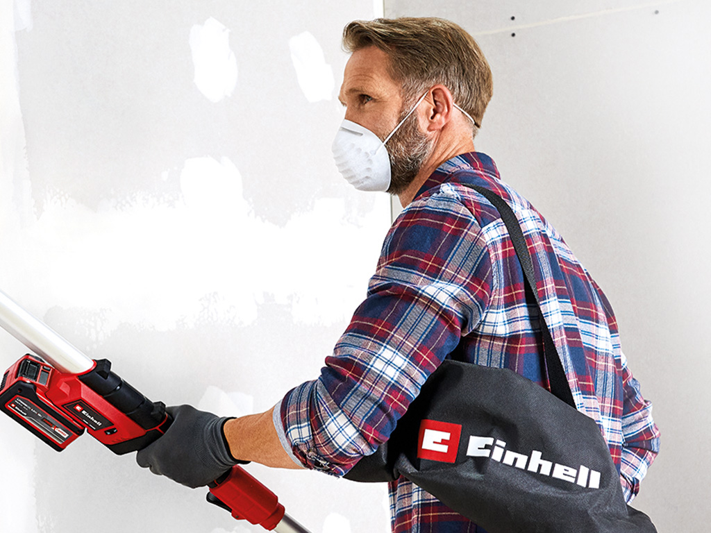 Man with battery-powered drywall grinder and protective mask