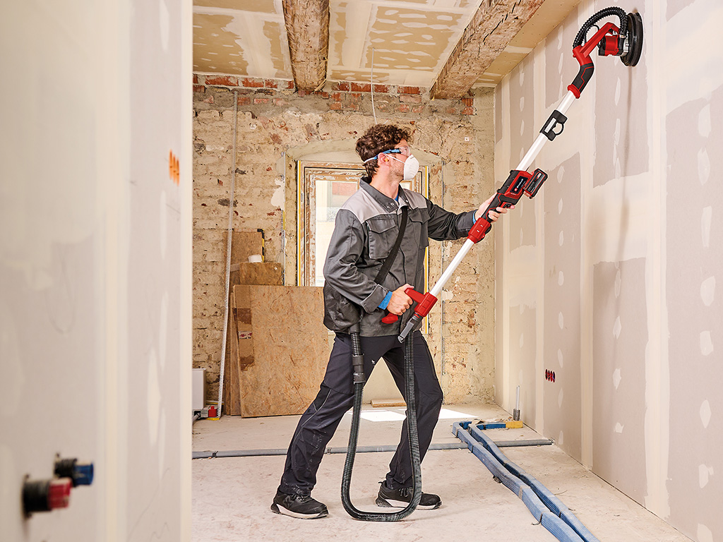 A man sanding a drywall with an Einhell drywall sander.