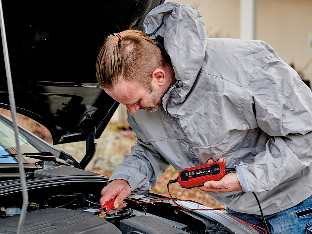 Man is using the Einhell battery charger to charge his car battery with the bonnet open.