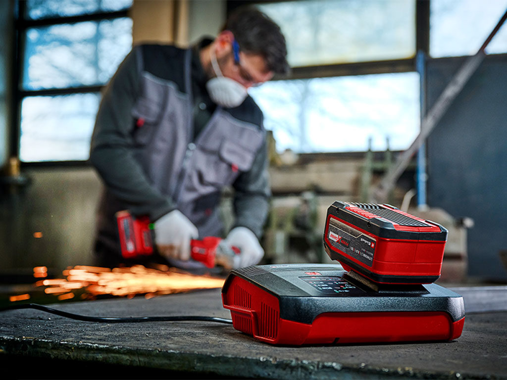 in the front: a Einhell battery charger | in the back: a man working with a cordless tool