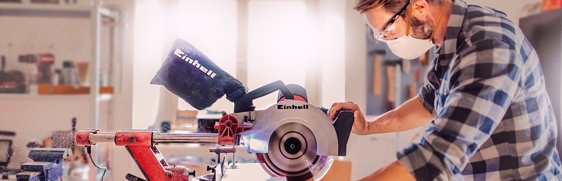 Ein Mann sägt in einer Werkstatt mit einer Einhell Kapp- und Gehrungssäge ein Holzbrett.