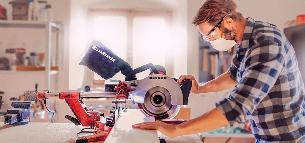 Ein Mann sägt in einer Werkstatt mit einer Einhell Kapp- und Gehrungssäge ein Holzbrett.