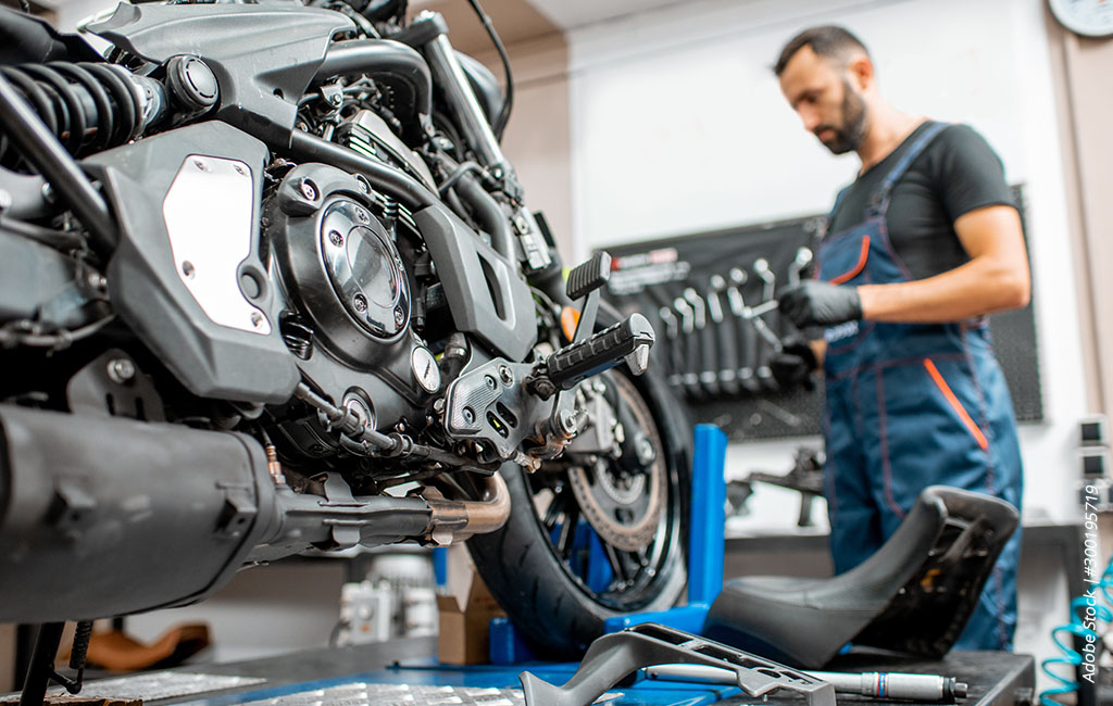 Motorcycle on a lift in a workshop while a person in the background prepares maintenance work.