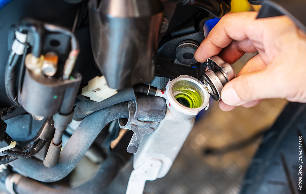 Hand opening the coolant reservoir of a motorcycle to check the fluid level.