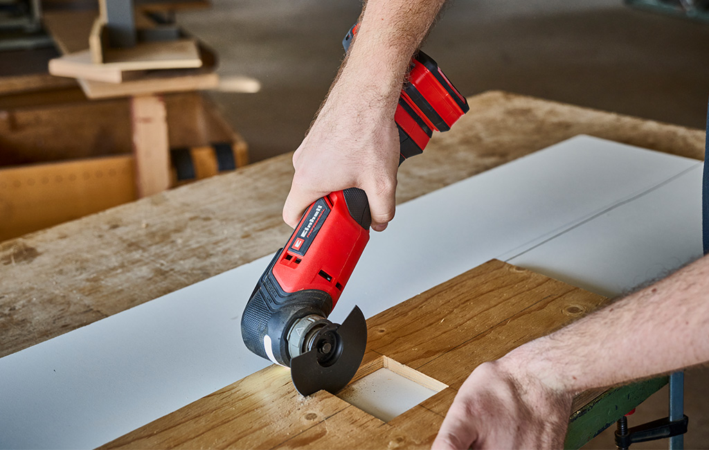 Close-up of hands cutting a notch in a wooden board with a Einhell cordless multitool.