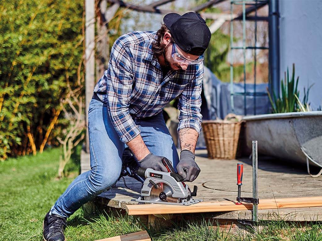 A man cuts a wooden board with a circular saw on the ground