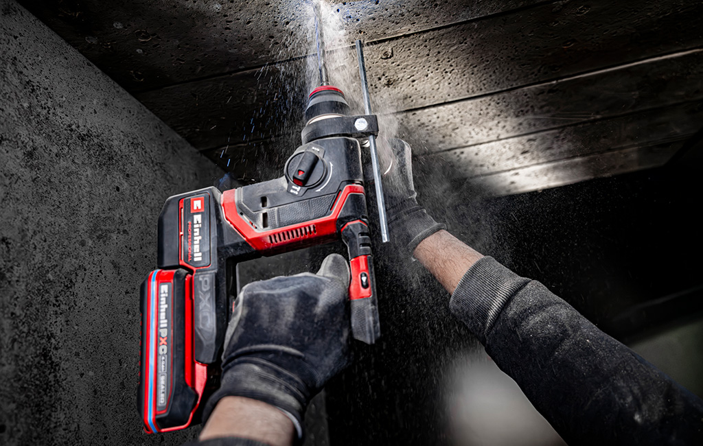 Cordless rotary hammer drilling into a concrete ceiling as drilling dust falls down.