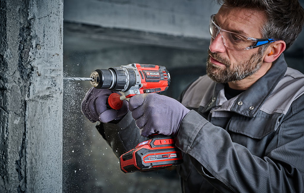 Man drilling into concrete with a cordless impact drill while wearing safety glasses and hearing protection.