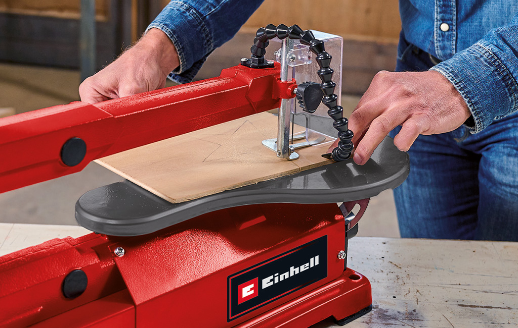 Ein Mann sägt mit der Einhell Dekupiersäge eine Form aus einer dünnen Holzplatte.