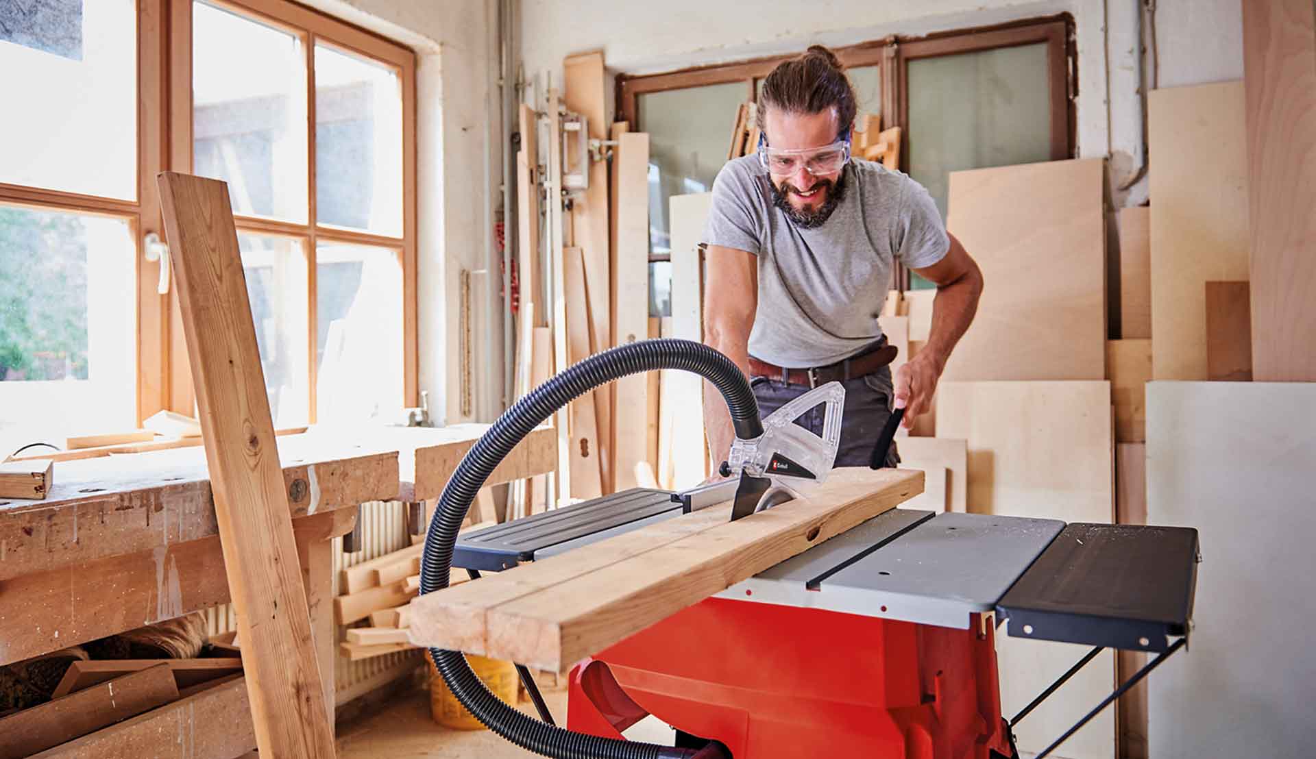 A man cutting a wooden plank with a red table saw.