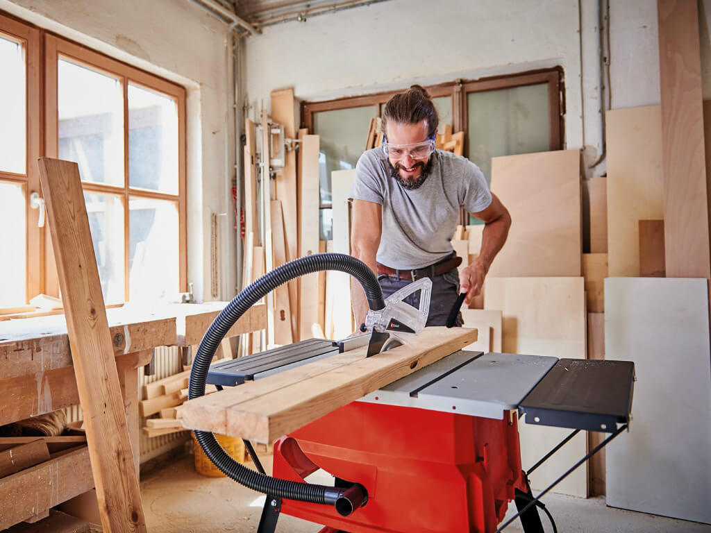 man cuts wooden board in two parts with a table saw