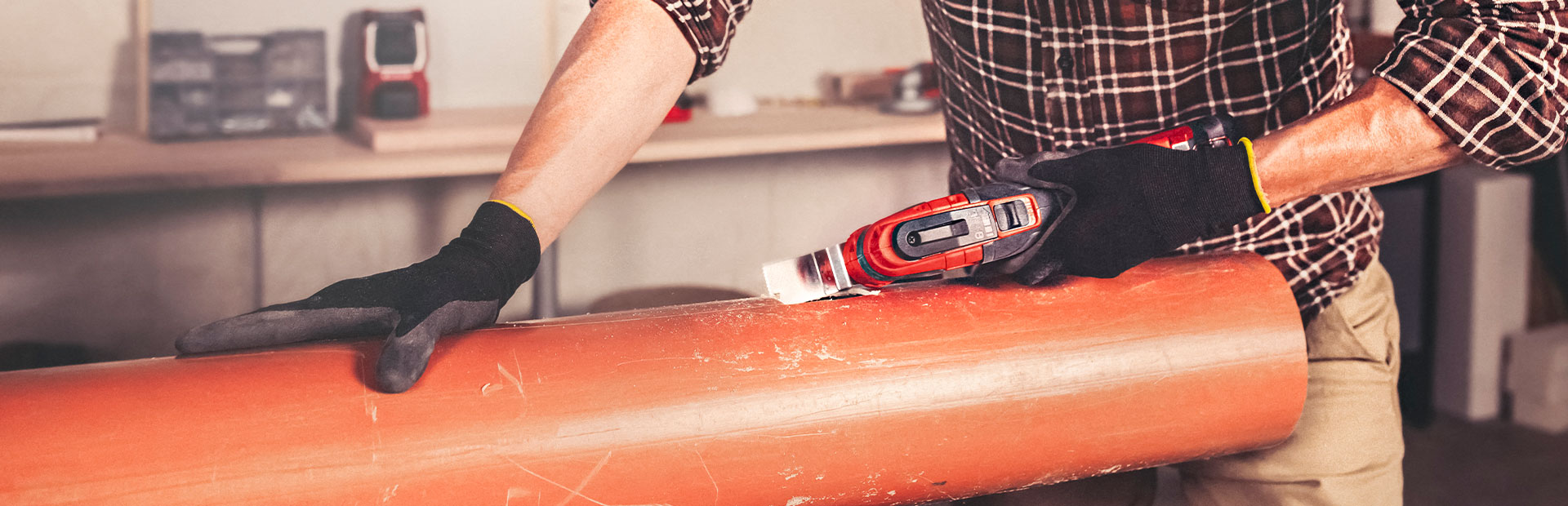 A man is cutting into a plastic pipe with a multifunctional tool.