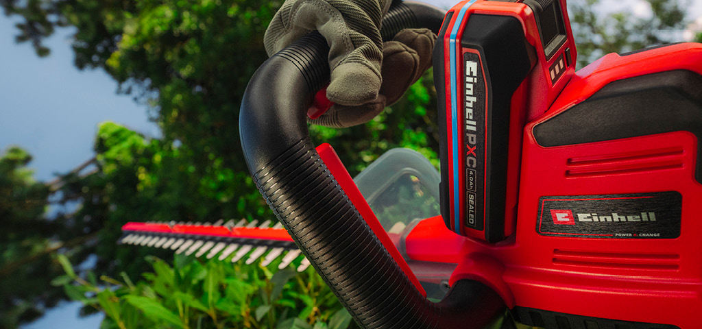 Einhell-Akku-Heckenschere schneidet eine Hecke im Garten.