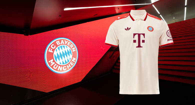 Ein cremefarbenes FC-Bayern-Trikot mit roten Details vor einer roten Wand mit FC-Bayern-Logo im Stadion-Innenbereich.