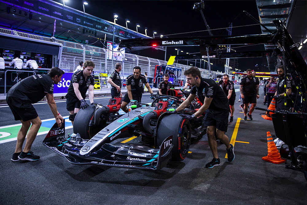 Several Mercedes-AMG PETRONAS F1 Team mechanics with a Formula 1 car in the pit lane at night.