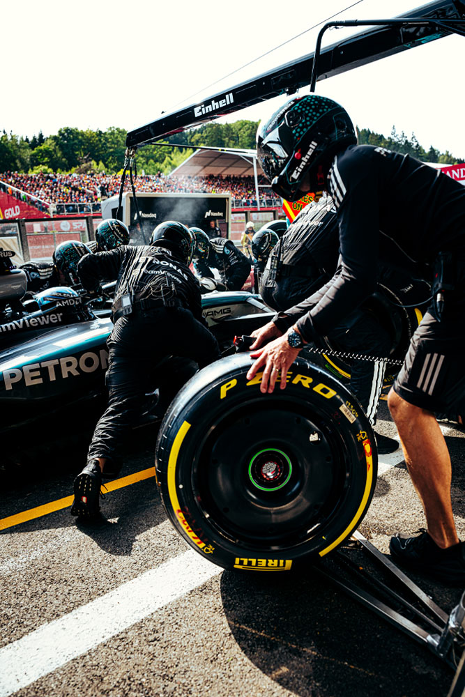 Mechaniker des Mercedes-AMG PETRONAS Formel-1-Teams führen einen Boxenstopp durch. Ein Teammitglied bereitet einen Pirelli-Reifen vor, während andere am Fahrzeug arbeiten. Das Einhell-Logo ist auf dem Equipment über dem Auto zu sehen.